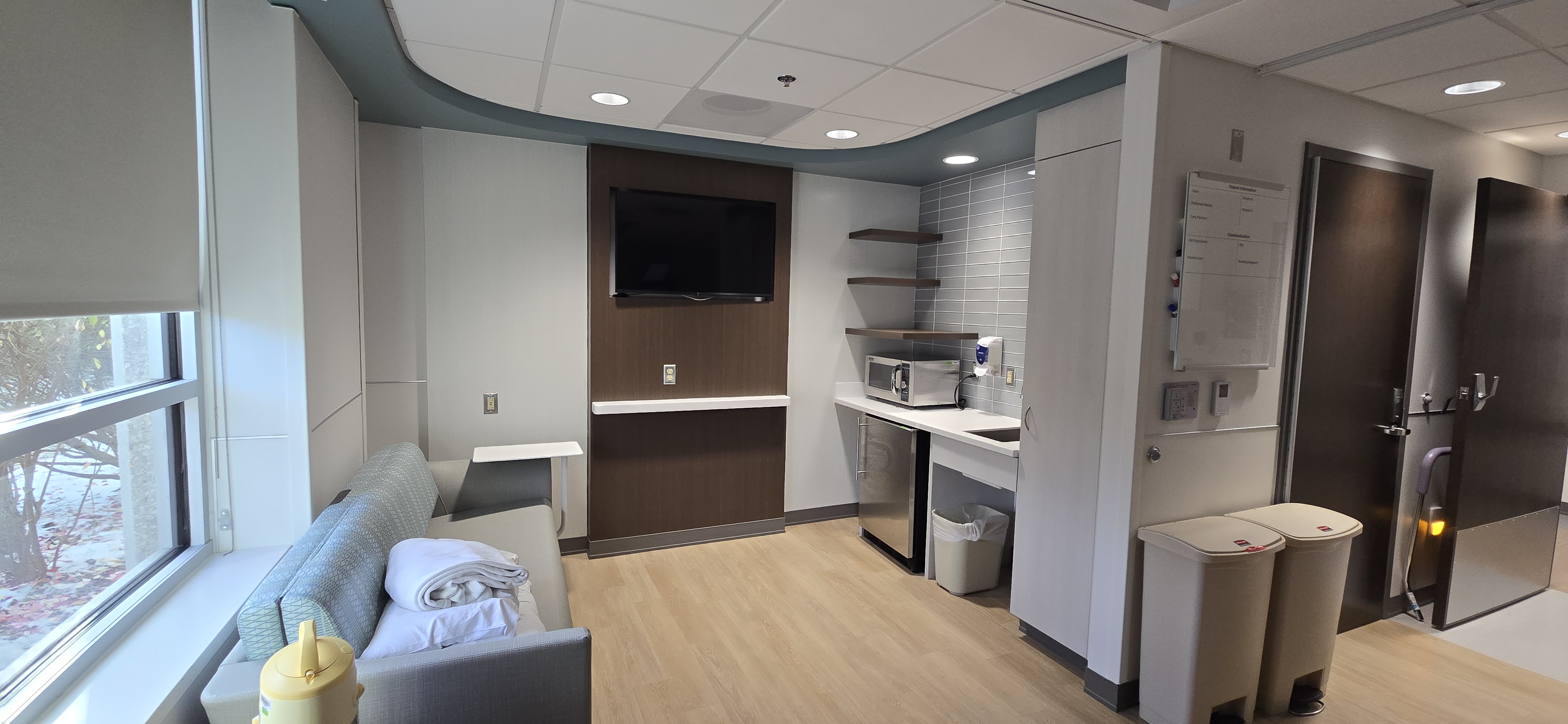 Family space in a hospital room with couch, tv, and refrigerator